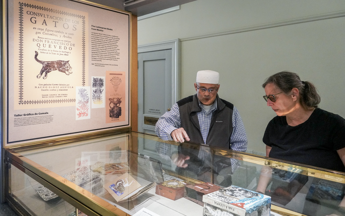 Two people talk over a glass exhibit case of books